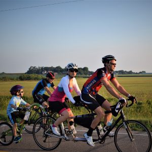 Here a family is having fun and making memories, on a tandem bike with a tag-along (a.k.a. trailer cycle or trail-a-bike), riding across Iowa, on RAGBRAI 2017.