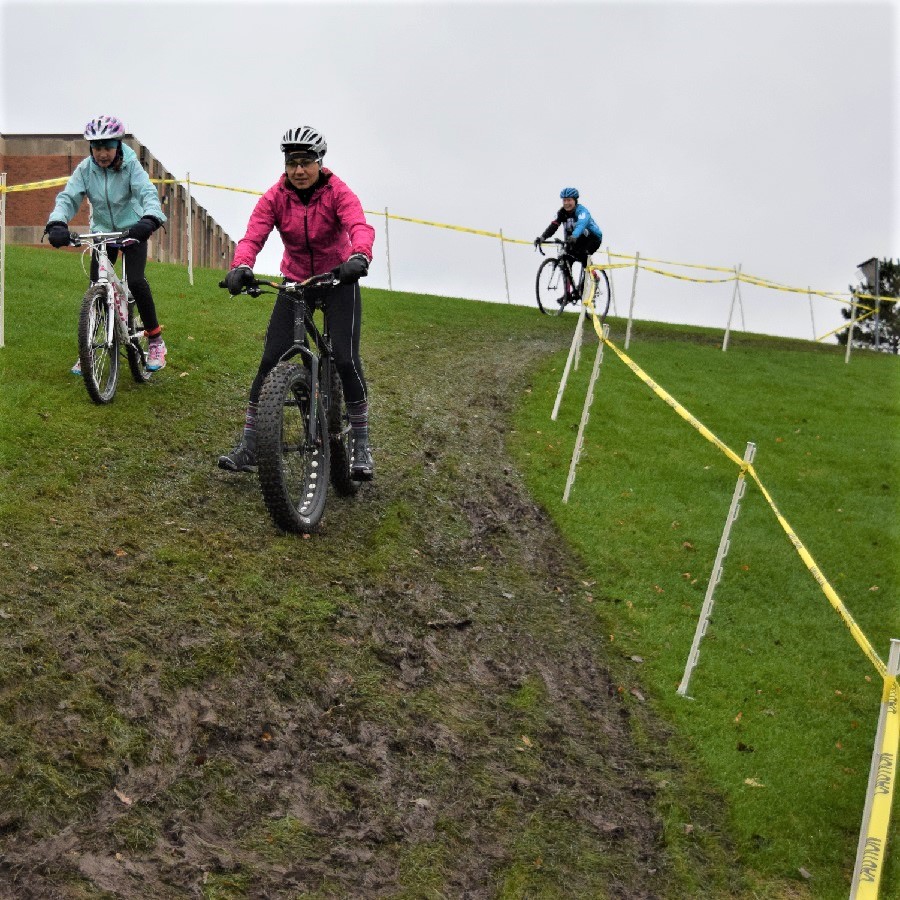 Here in the forefront a amateur rider tests out the muddy cycle-cross course with a fat bike.