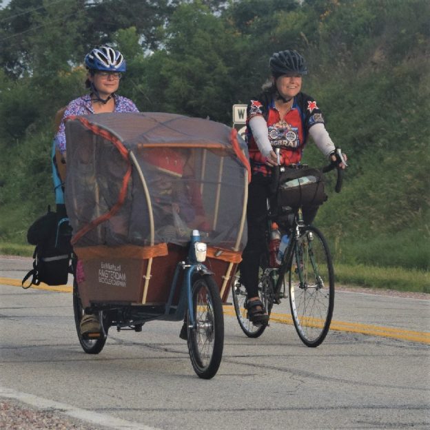 Looks a beautiful sunny day, here in this bike pic we captured a biker chick peacefully riding a cargo bike, from Amsterdam, with her child inside. This picture was captured on a picture perfect day riding across Iowa on RAGBRAI 2018.